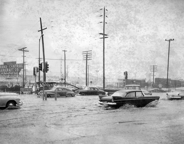1938: People walk along the flooded L.A. River near the Dayton Avenue Bridge. In the background, a railroad bridge hangs in a twisted heap after one of the pilings has collapsed. (Photograph courtesy of the Los Angeles Public Library)