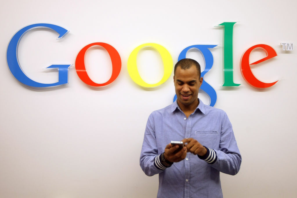 Google Opens New Berlin Office A visitor uses a cell phone in front of the Google logo on September 26, 2012 at the official opening party of the Google offices in Berlin, Germany.