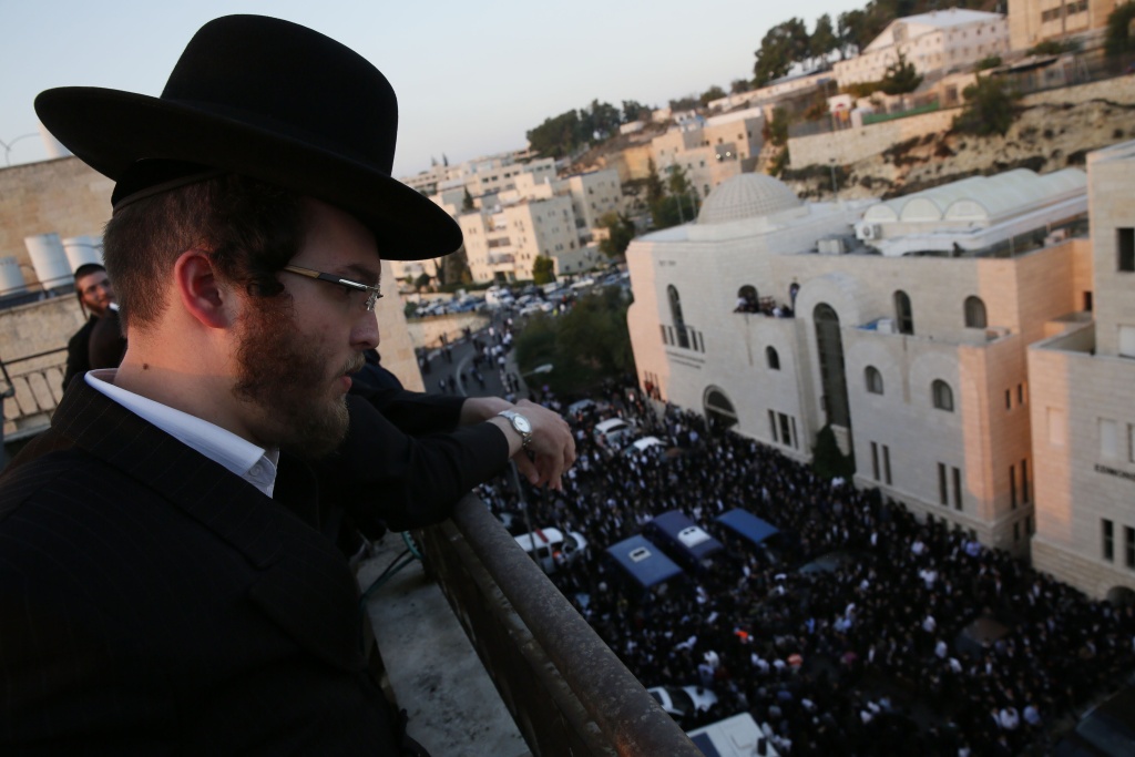 ISRAEL-PALESTINIAN-CONFLICT-JERUSALEM-SYNAGOGUE An Ultra-Orthodox Jew looks down from a roof top over people mourning near the bodies of the victims of an attack by two Palestinians on Jewish worshippers killing four Israelis at a synagogue in the Ultra-Orthodox Har Nof neighbourhood in Jerusalem, at the site where the attack took place on November 18, 2014. Two Palestinians armed with a gun and axes burst into a Jerusalem synagogue and killed four Israelis before being shot dead, in the deadliest attack in the city in years.