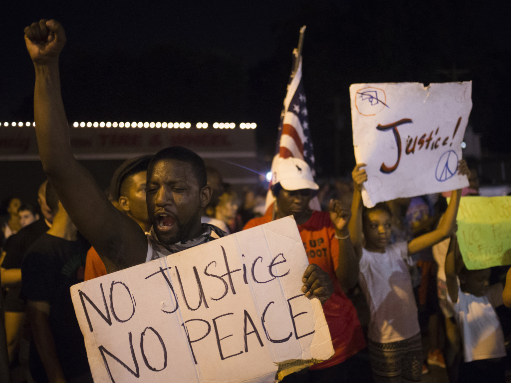Demonstrators protest the killing of unarmed 18-year-old Michael Brown across the street from the Ferguson Police Department in Ferguson, Mo., Friday night. More than a week of unrest has largely given way to peaceful protests recently. Demonstrators protest the killing of unarmed 18-year-old Michael Brown across the street from the Ferguson Police Department in Ferguson, Mo.