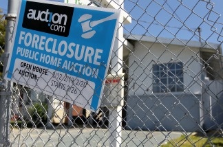 A foreclosure sign hangs on a fence in front of a foreclosed home in California.