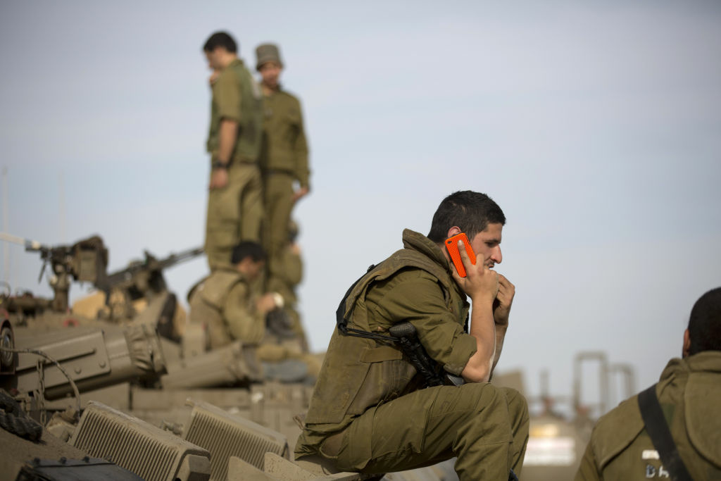 ISRAEL-PALESTINIAN-CONFLICT-GAZA An Israeli soldier talks on his mobile phone as he sits on top of an armoured personnel carrier (APC) stationed on Israel's border with the Gaza Strip on November 16, 2012. Israeli officials said the Jewish state was preparing to launch its first ground offensive in four years into the Gaza Strip and the army started calling up reservists.