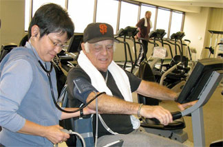 Actor Jonathan Haze bicycles at the Cardiac Rehab Lab at Cedars-Sinai Heart Institute. Exercise physiologist Asako Oshiro takes his blood pressure while he’s pumping.