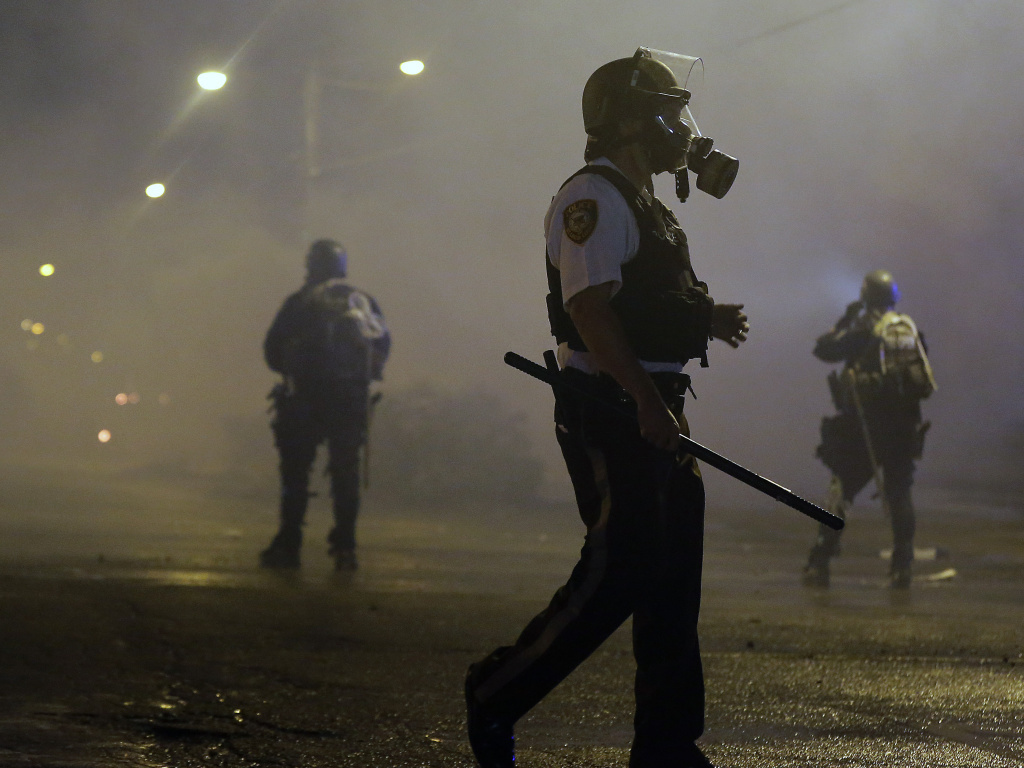 Law enforcement officers wait to advance Sunday morning after firing tear gas to disperse a crowd protesting the shooting of teenager Michael Brown in Ferguson, Mo. Authorities report one shooting and several arrests. Law enforcement officers wait to advance Sunday morning after firing tear gas to disperse a crowd protesting the shooting of teenager Michael Brown in Ferguson, Mo. Authorities report one shooting and several arrests.