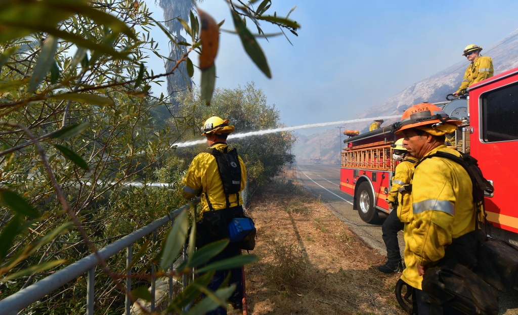 Firefighters douse flames and smoke near homes in West Hills, California on November 11, 2018, as they continue their battle to control the Woolsey Fire. Firefighters douse flames and smoke near homes in West Hills, California on November 11, 2018, as they continue their battle to control the Woolsey Fire. - Near Los Angeles, where the fire is threatening mansions and mobile homes alike in the coastal celebrity redoubt of Malibu, the death toll has so far been limited to two victims found in a vehicle on a private driveway. (Photo by Frederic J. BROWN / AFP) (Photo credit should read FREDERIC J. BROWN/AFP/Getty Images)