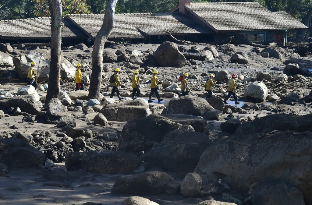 US-WEATHER-MUDSLIDES A firefighting handcrew walks past debris near a property buried in mud in Montecito, California January 12, 2018.