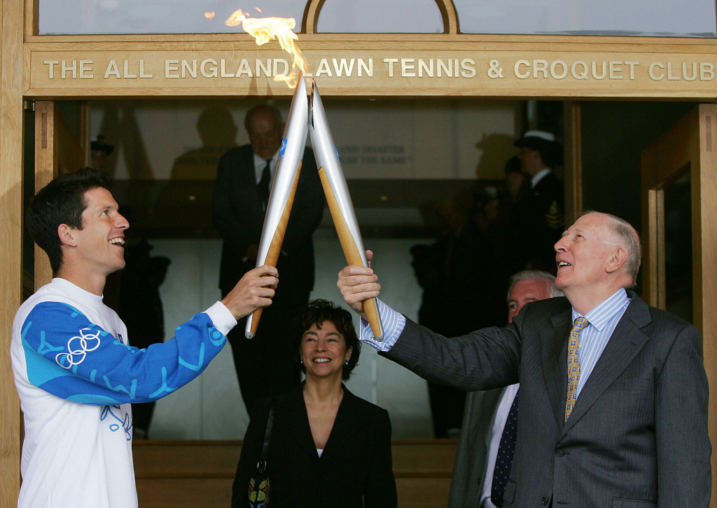 Tennis player Tim Henman (L) of Great Br Tennis player Tim Henman (L) of Great Britain has receives the Olympic flame from Sir Roger Bannister after a lighting ceremony on the Centre Court of Wimbledon in London, 26 June, 2004.