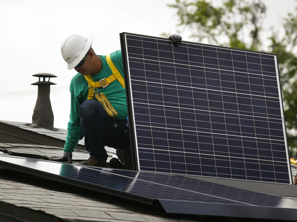 A SolarCity employee installs a solar panel on the roof of a home in Los Angeles in 2014. California's utilities want to pay new solar customers less for their extra electricity and to add new monthly fees. A SolarCity employee installs a solar panel on the roof of a home in Los Angeles in 2014. California's utilities want to pay new solar customers less for their extra electricity and to add new monthly fees.