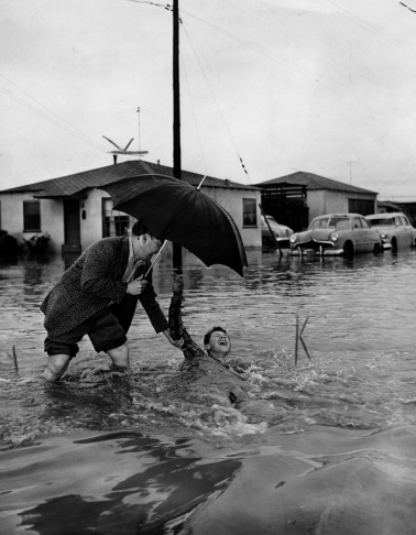 1938: People walk along the flooded L.A. River near the Dayton Avenue Bridge. In the background, a railroad bridge hangs in a twisted heap after one of the pilings has collapsed. (Photograph courtesy of the Los Angeles Public Library)