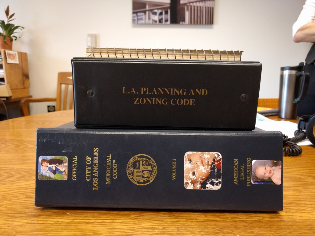 The 3-inch binder on the bottom is what the LA city planning code looks like now. The one in the middle is what it was in 2002. And the small spiral-bound book on the top is what it looked like in 1966. The 3-inch binder on the bottom is what the LA city planning code looks like now. The one in the middle is what it was in 2002. And the small spiral-bound book on the top is what it looked like in 1966.