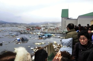 Local residents watch the devastation provoked by a tsunami tidal wave smashing vehicles and houses at Kesennuma city in Miyagi prefecture, northern Japan on March 11, 2011.