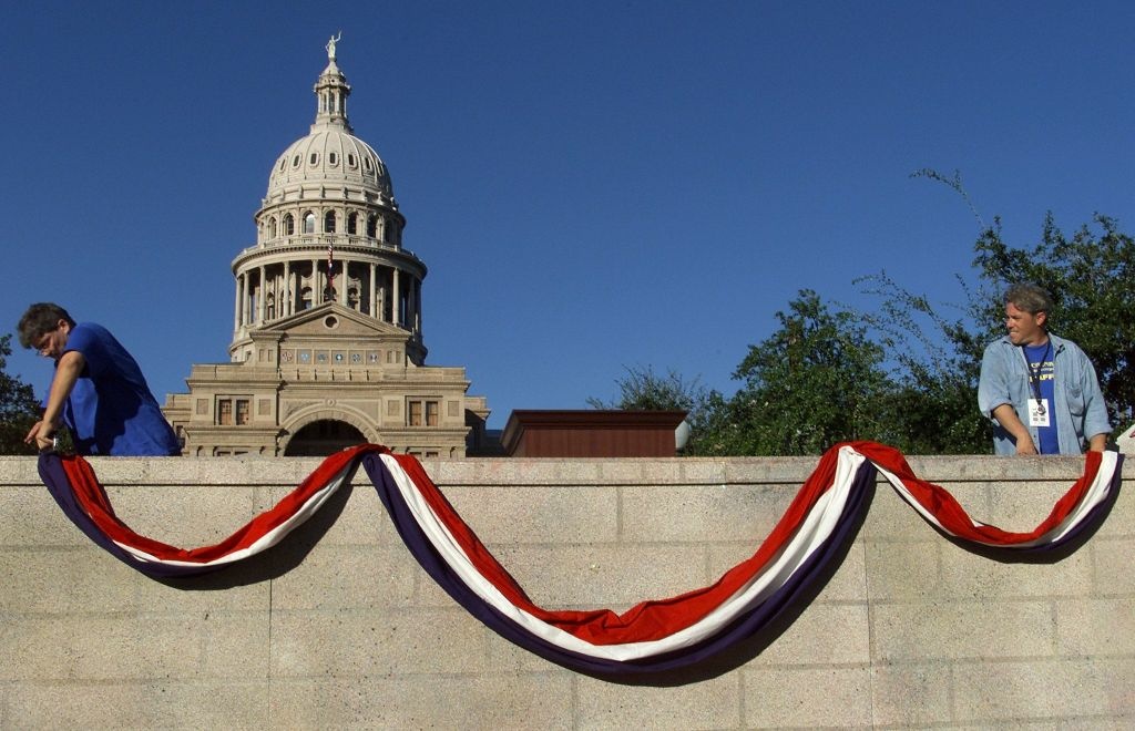 Production crew workers Faith Schexnayder (L) and Production crew workers hang red, white and blue bunting on the stage with the Texas Capitol Building in the background.