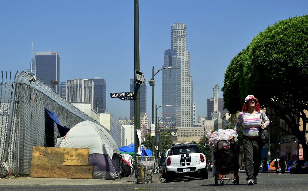 US-HOMELESSNESS-CALIFORNIA-VETERANS A woman pushes her cart full of belongings along the street past tents on the sidewalk near Skid Row in downtown Los Angeles, California on June 20, 2017.