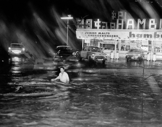 1938: People walk along the flooded L.A. River near the Dayton Avenue Bridge. In the background, a railroad bridge hangs in a twisted heap after one of the pilings has collapsed. (Photograph courtesy of the Los Angeles Public Library)