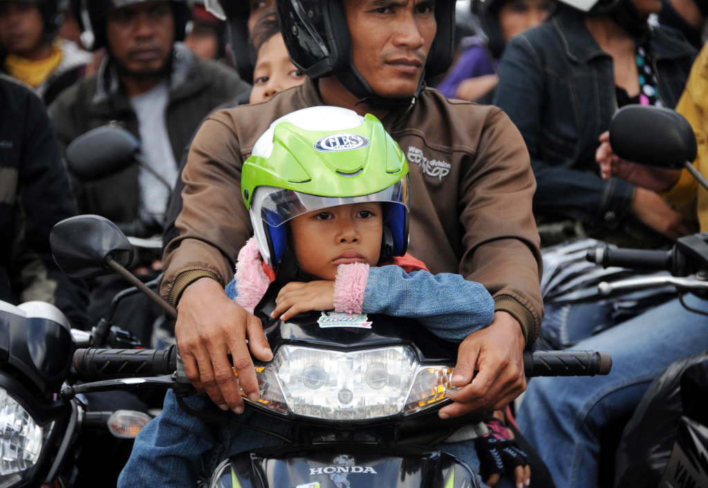 A young boy sits with his family on a mo A young boy sits with his family on a motorbike as motorists wait to board a ferry headed for Java from the port of Gilimanuk in Jembrana on the mainly Hindu resort island of Bali on August 28, 2011.