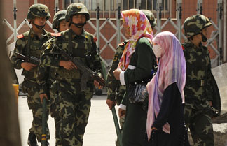 Muslim ethnic Uighur women pass a Chinese paramilatary police on patrol on a street in Urumqi, capital of China's Xinjiang region on July 3, 2010 ahead of the first anniversary of bloody violence that erupted between the region's Muslim ethnic Uighurs and members of China's majority Han ethnicity.