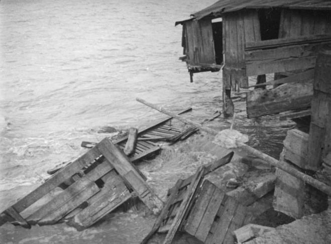 1938: People walk along the flooded L.A. River near the Dayton Avenue Bridge. In the background, a railroad bridge hangs in a twisted heap after one of the pilings has collapsed. (Photograph courtesy of the Los Angeles Public Library)