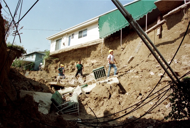 1938: People walk along the flooded L.A. River near the Dayton Avenue Bridge. In the background, a railroad bridge hangs in a twisted heap after one of the pilings has collapsed. (Photograph courtesy of the Los Angeles Public Library)
