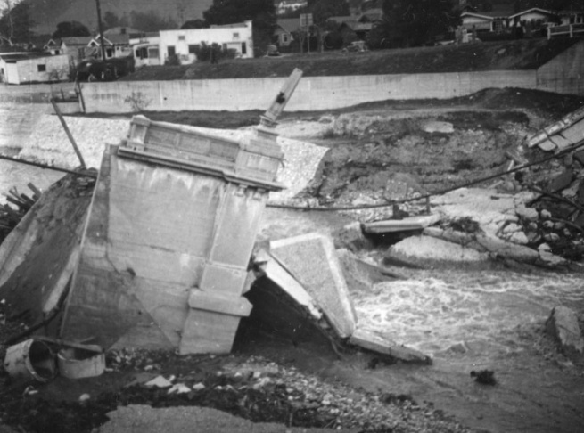 1938: People walk along the flooded L.A. River near the Dayton Avenue Bridge. In the background, a railroad bridge hangs in a twisted heap after one of the pilings has collapsed. (Photograph courtesy of the Los Angeles Public Library)