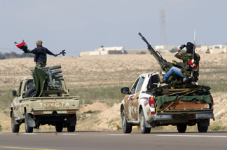 Rebel fighters drives towards the university (background) of the key old port of Brega on their way to battle against loyalist troops on April 4, 2011.