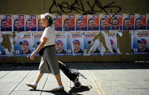 A women passes by in front of propaganda posters of Venezuelan President and candidate Hugo Chavez (top) and opposition presidential candidate Henrique Capriles, in Caracas on October 5, 2012. Elections in Venezuela will be held on October 7.