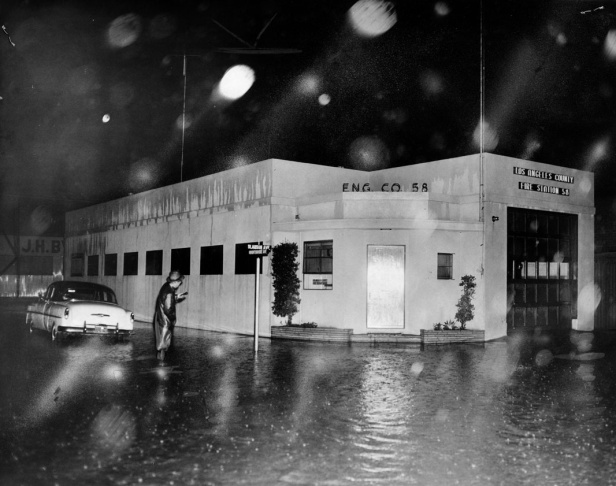 1938: People walk along the flooded L.A. River near the Dayton Avenue Bridge. In the background, a railroad bridge hangs in a twisted heap after one of the pilings has collapsed. (Photograph courtesy of the Los Angeles Public Library)