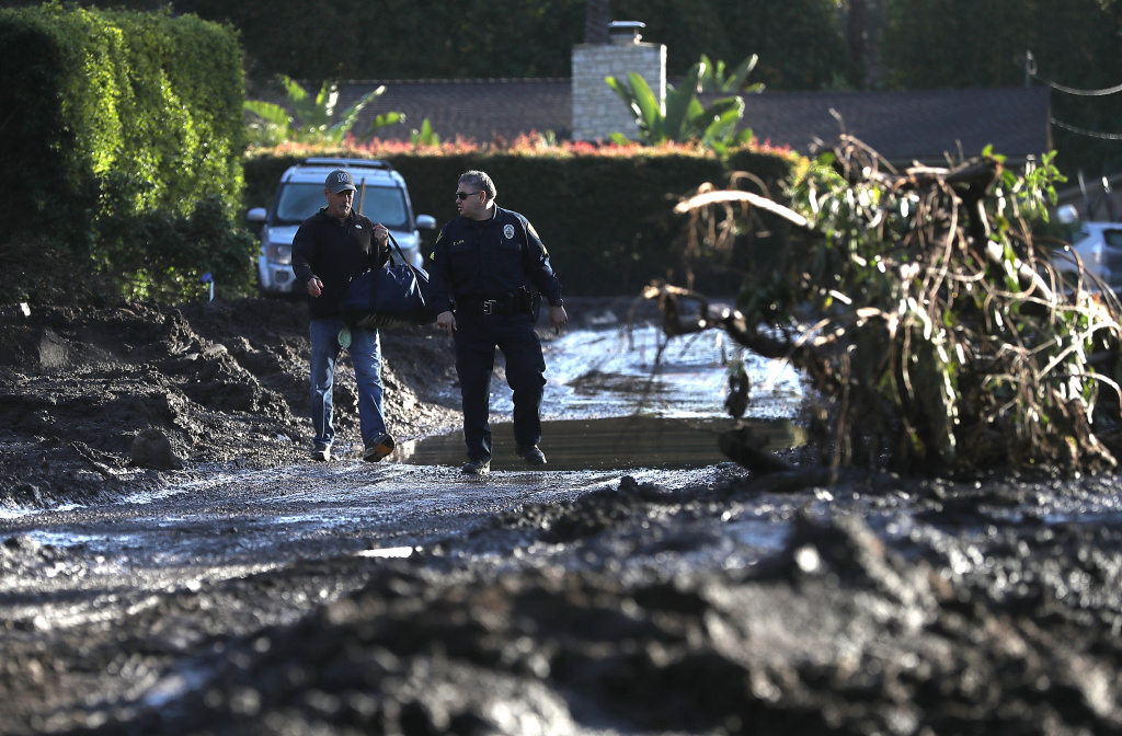 Mudslides Kill At Least 17 People In Santa Barbara County Where Wildfire Scorched Hillside A police officer escorts a resident through a neighborhood that was destroyed by a mudslide on January 12, 2018 in Montecito, California.